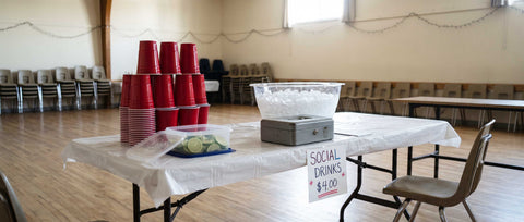 Bar table set up for a Manitoba social with plastic cups, an ice tub and a cash box